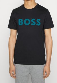 Svart bomull t-shirt med en djärv turkos "BOSS" logotyp på framsidan, rund krage och korta ärmar. Slät textur, figursydd design.