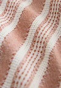 Textil mit abwechselnden Pfirsich- und weißen Streifen, das eine gewebte Textur mit offenen Mustern und einem weichen Erscheinungsbild aufweist.