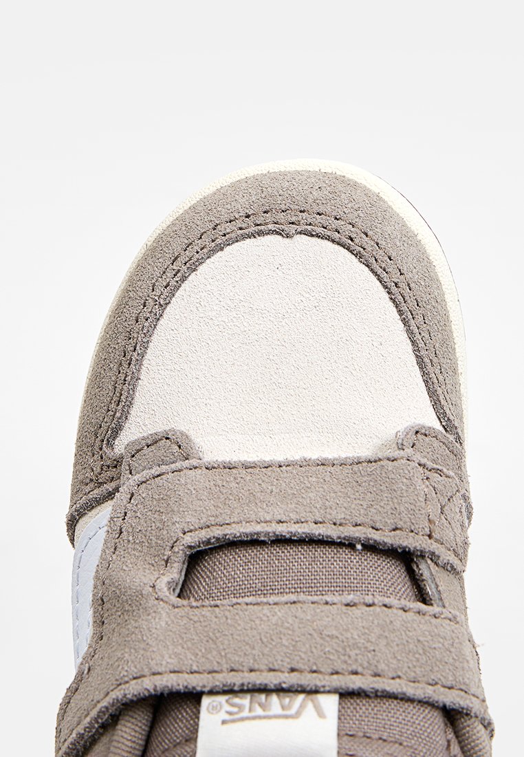 Braune Wildledersneaker mit weißen Akzenten, Klettverschluss, strukturiertem Material, abgerundetem Zehenbereich und sichtbaren Steppnähten.