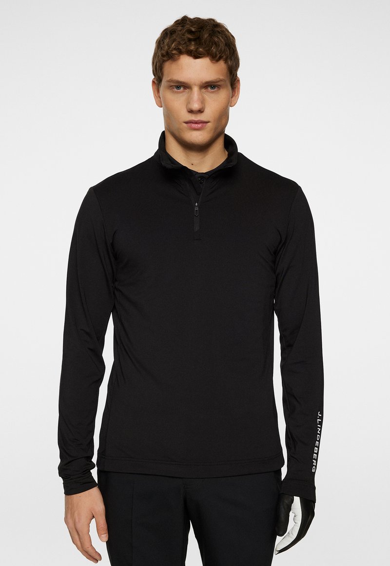 Mustapaita, jossa on pitkät hihat ja puolivetoketju-kaulus, sileä rakenne, vasemmassa hihassa logo ja muotoiltu malli.