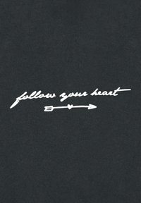 Tessuto nero con testo in bianco che recita "segui il tuo cuore", accompagnato da una semplice freccia e un grafico a forma di cuore.