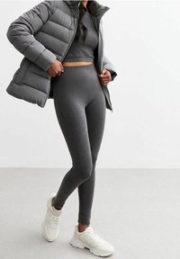 Chaqueta acolchada gris sobre un top recortado de canalé a juego y leggings, con un diseño ajustado. Completado con zapatillas deportivas blancas.