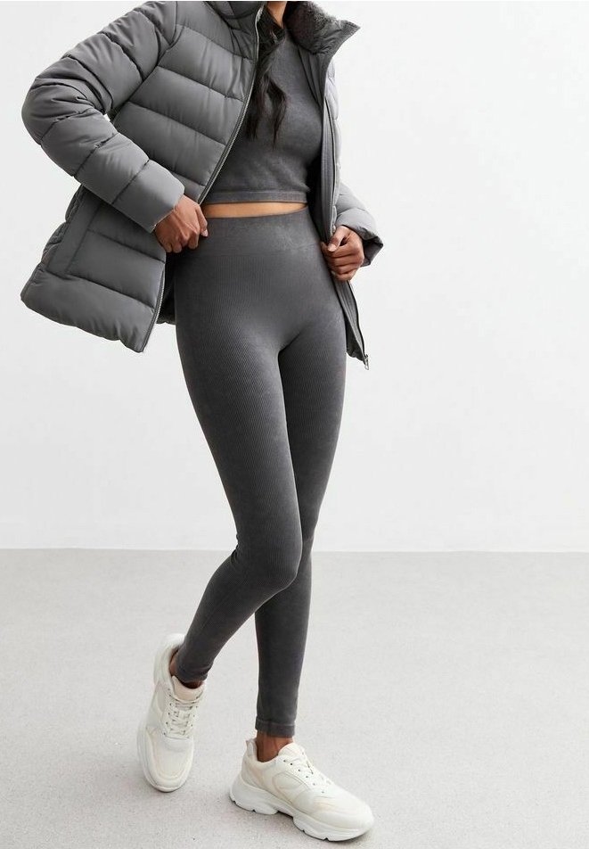 Chaqueta acolchada gris sobre un top recortado de canalé a juego y leggings, con un diseño ajustado. Completado con zapatillas deportivas blancas.