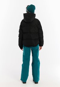 Zwarte gewatteerde jas met een capuchon, gecombineerd met teal skibroek. De jas heeft een geborduurd ontwerp en elastische manchetten.