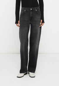 Blugi negri din denim cu croială largă, finisaj cu aspect estompat, design cu cinci buzunare și închidere cu nasture metalic. Se remarcă prin textura netedă și croiala dreaptă.