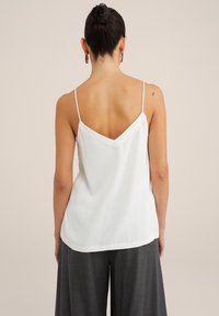 White satin camisole with thin straps, a V-shaped back, and a smooth texture. Paired with gray wide-leg trousers.