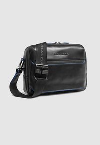 Zwarte leren schoudertas met blauwe accentstiksels, verstelbare schouderriem en een voorvak met rits, met een gladde textuur en rechthoekige vorm.