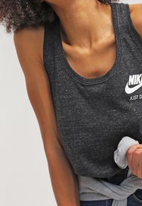 Svart ärmlös tank top tillverkad av texturerad tyg, med en vit Nike-logotyp på bröstet. Materialet verkar vara lätt och andningsbart.