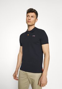 Granatowa koszulka polo z kołnierzykiem, krótkimi rękawami, pomarańczowymi guzikami i małym czerwonym logo na klatce piersiowej. Gładki bawełniany materiał.