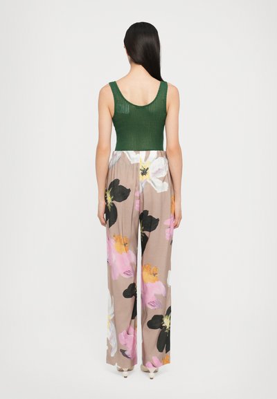 Top senza maniche a coste verdi abbinato a pantaloni ampi a fiori con motivi rosa, neri e gialli su sfondo beige.