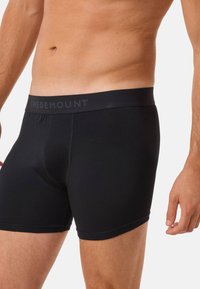 Man wearing black Swedemount boxer briefs, showing lower torso and upper legs against a plain light background.