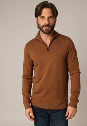 Pull marron à col zippé avec manches longues, poignets et ourlet côtelés, fabriqué en maille douce. Porté avec un jean bleu.