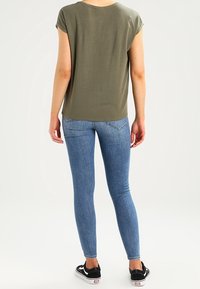 Luźna oliwkowa bluzka z rolowanymi rękawami, zestawiona z obcisłymi niebieskimi dżinsami. Czarne trampki z białymi akcentami.