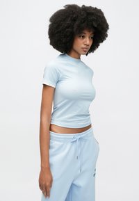 Jasnoniebieska dopasowana sportowa koszulka z krótkimi rękawami, okrągłym dekoltem i gładką fakturą, zestawiona z dopasowanymi jasnoniebieskimi dresami z elastycznym paskiem w talii.