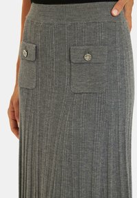 Jupe maxi grise côtelée avec une large taille, deux poches avant, chacune avec un bouton décoratif, fabriquée en tissu doux et extensible.