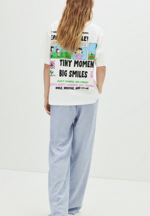 T-shirt bianco oversize con grafiche e testo a fumetti colorati. Abbinato a pantaloni larghi a strisce azzurre, che mostrano una vestibilità rilassata.