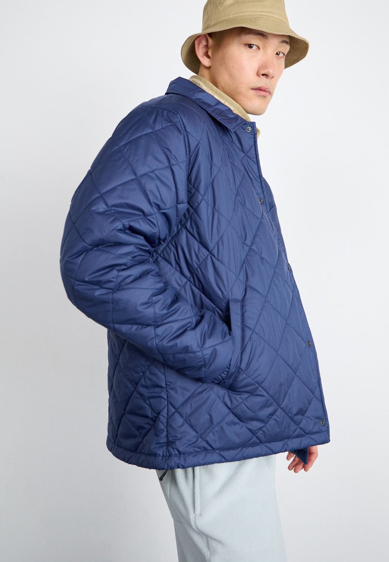 Veste matelassée bleu marine avec une fermeture à boutons et des poches latérales, présentant un col classique et une coupe décontractée.