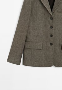 Harmaa houndstooth-takki, jossa on viistetty kaulus, neljä mustaa nappia ja kaksi etutaskua. Teksturoitu kangas ja muotoiltu istuvuus.