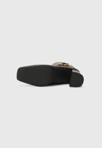 Brown leather shoe with a circular gold accent and textured black sole. Features a low block heel for stable support and rounded toe design.