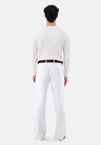 Weißer, kabelgestrickter Pullover mit rundem Halsausschnitt, kombiniert mit weit geschnittenen weißen Hosen und einem dunkelbraunen Gürtel. Glattes Material mit strukturiertem Muster.