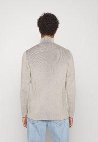 Beige gerippter Pullover mit hohem Kragen und langen Ärmeln, ausgestattet mit einem strukturierten Strickdesign und seitlichen Schlitzen am Saum.