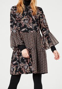 Černé šaty s paisley vzorem, rozšířenými rukávy a patrovým lemem. Disponují vzorovanou spodní částí a jednobarevným černým límcem.