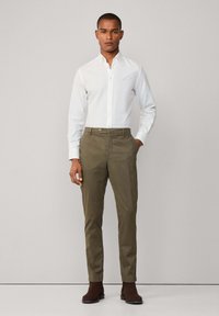 Camisa blanca de cuello y pantalones de color verde oliva, con un corte ajustado, textura suave y cierre de botón en la cintura. Botines marrones.
