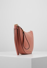 Pink læderhåndtaske i rund form, med en glat tekstur, strukturerede sidepaneler og detaljer med guldfarvet hardwarelogo.