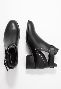 Botas de cuero negras hasta el tobillo con tachuelas plateadas, tacones de bloque y recortes laterales; una bota vista desde arriba, la otra desde un lado.