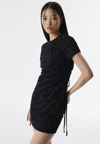 Zwarte jurk met een tekstpatroon, korte mouwen en geraffineerde zijkanten met verstelbare strikken. Gladde stof met een slim fit ontwerp.
