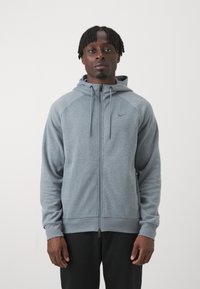 Gray zip-up hoodie with a soft texture, featuring a front zipper, drawstring hood, and contrasting shoulder seams. Nike logo on chest.