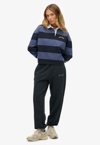 Suéter a rayas en tonos azules con cuello blanco y logotipo, combinado con pantalones de chándal negros con logotipo. Tejido ligero, ajuste relajado.