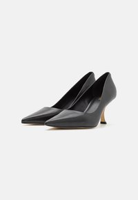 Escarpins en cuir noir à bout pointu avec un talon fin orné d'un accent doré. Texture lisse avec une silhouette élégante et un design minimaliste.