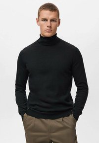 Schwarzer Rollkragenpullover aus weichem, leichtem Stoff, mit langenÄrmeln und taillierter Passform. Kombiniert mit beigen Hosen.