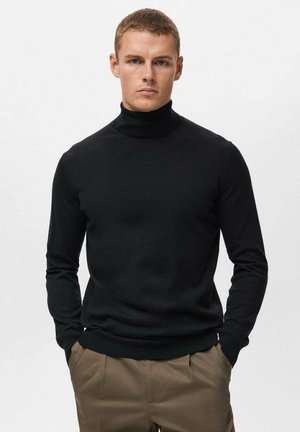 Maglione nero a collo alto realizzato in tessuto morbido e leggero, con maniche lunghe e un design aderente. Indossato con pantaloni beige.