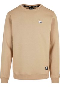 Sweat-shirt beige à col rond avec manches longues, poignets et ourlet côtelés, présentant de petits logos d'étoiles noirs et blancs sur la poitrine et l'ourlet inférieur.