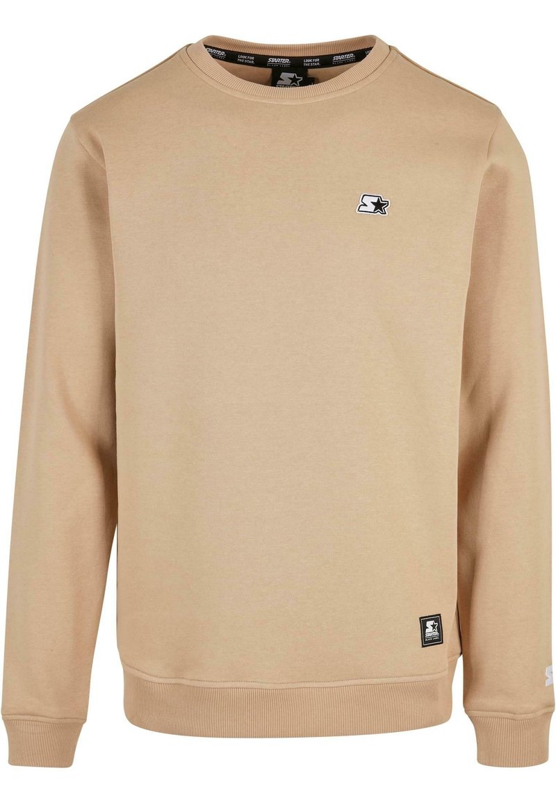 Sweat-shirt beige à col rond avec manches longues, poignets et ourlet côtelés, présentant de petits logos d'étoiles noirs et blancs sur la poitrine et l'ourlet inférieur.