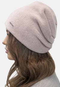Gorro de punto rosa con una textura suave, que presenta un diseño holgado y un pequeño acento metálico con el logo en el lateral.