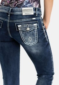 Dunkelblaue Denim-Jeans mit aufwändiger Stickerei auf den hinteren Taschen, kontrastierenden Nähten und einem Marken-Patch mit Nieten am Bund.