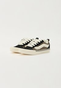 Sorte og brune sneakers med leopardprint-design, der har hvide snørebånd og en tekstureret gummisål. Accentueret med kontrasterende syninger.