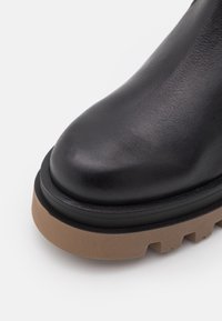 Bottines en cuir noir à bout arrondi, avec un dessus texturé et une semelle en caoutchouc beige épaisse avec un motif de traction visible.