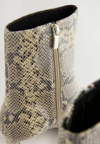 Cizme sintetice bej și gri până la gleznă cu un model de piele de șarpe, dotate cu un fermoar lateral și un căptușel interior moale de culoare neagră.