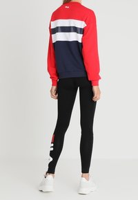 Sudadera de cuello redondo roja y marina con rayas horizontales, combinada con leggings negros que presentan gráficos en blanco y rojo, y zapatillas blancas.