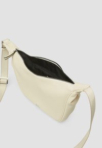 Cremefarbene Leder-Crossbody-Tasche mit strukturierter Oberfläche, Reißverschlussöffnung, verstellbarem Einzelgurt und schwarer Innenausstattung.