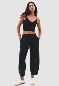Černý krátký top na ramínka s tenkými pásky, který je spárován s černými volnými kalhotami s bočními kapsami. Model má na sobě bílé tenisky.