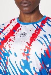 Sportovní tričko s krátkým rukávem, které má modro-červenobílý abstraktní vzor, kulatý výstřih a texturovanou látku. Logo je umístěno uprostřed.