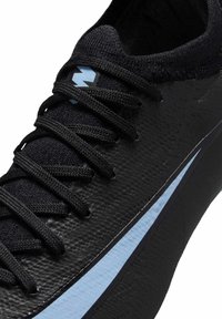 Zapatilla deportiva negra con upper texturizado, cordones negros y una franja de acento azul claro a lo largo del costado. Vista en primer plano del diseño.