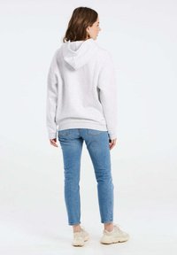 Felpa grigia con cappuccio, dal taglio rilassato, con polsini e orlo a coste, abbinata a jeans skinny azzurri e sneakers beige.