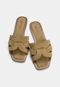 Tan suede slide sandals with a woven strap design, square toe, and a brown rubber sole. Flat with no heel elevation.