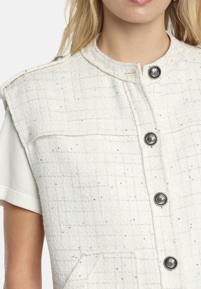 Witte textuurvest met een ruitpatroon, voorzien van zilveren pailletten, een opstaande kraag en donkere knopen aan de voorkant.